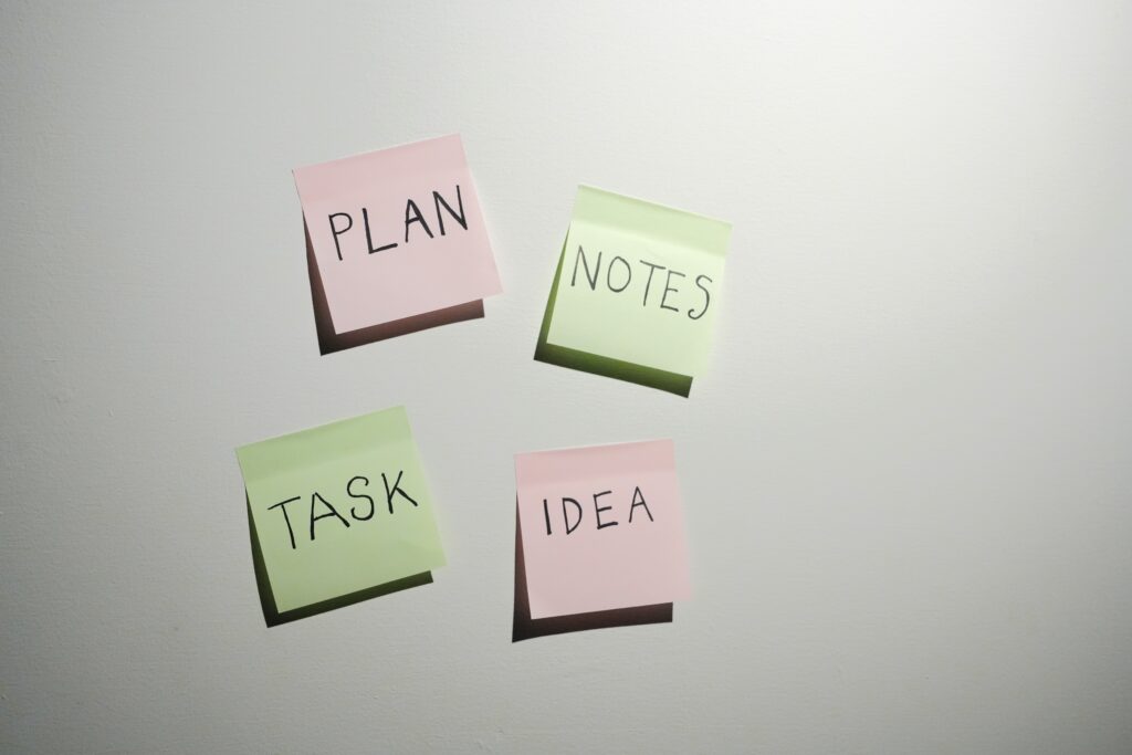 「PLAN NOTES TASK IDEA」と書かれた付箋が白い壁に2列に貼られており、左上はピンク、それ以外は緑色である