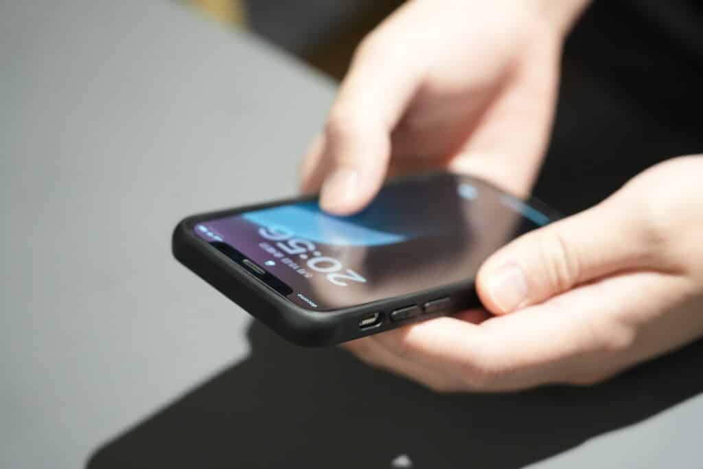 黒いケースに入った、両手でスマートフォンを持ち、親指で画面を操作している人
