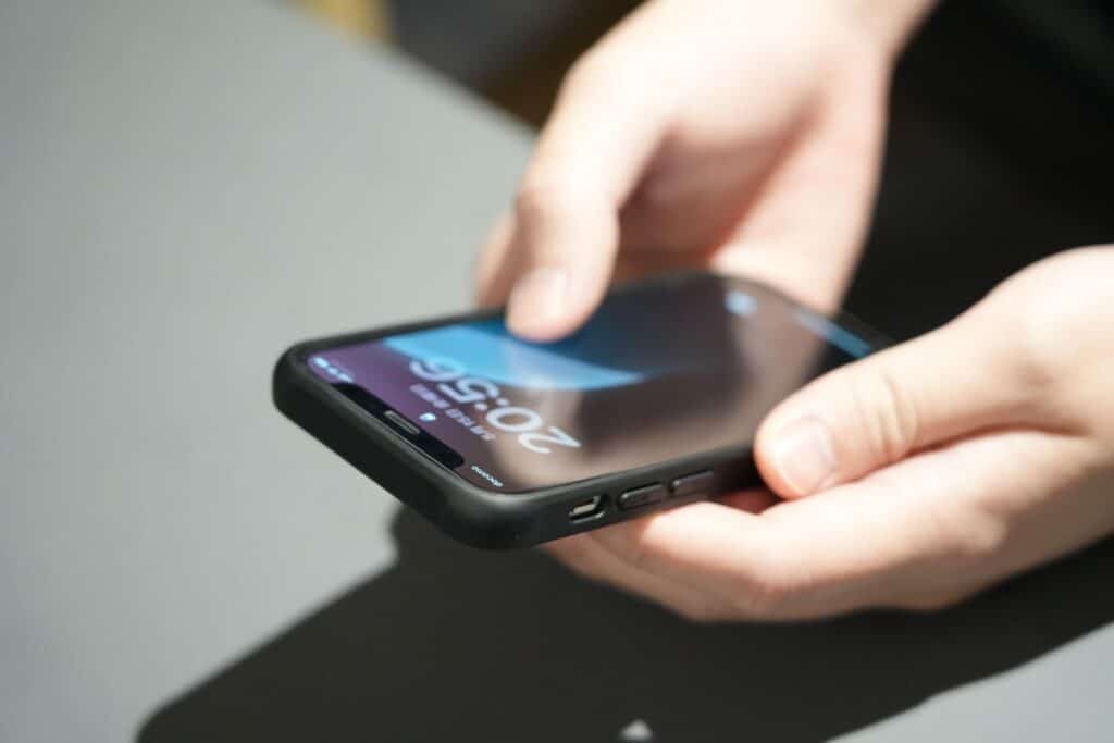 人が両手でスマホを持ち画面に20:56と黒い表示ケースでグレーの面に置かれている.