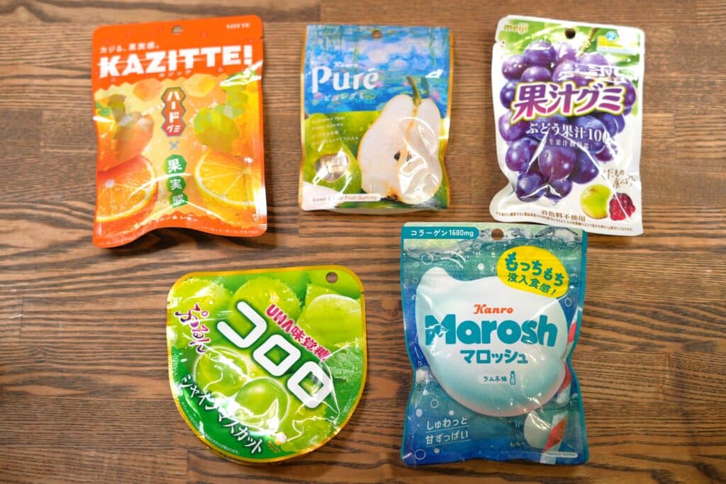 日本のグミ5袋が木の上に並んでおり、パッケージにはブドウや柑橘類の果物が描かれている